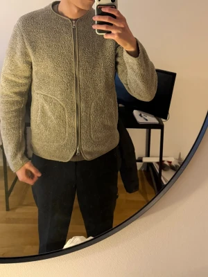 J. Lindeberg Beige Ull Herr S - Säljer en beige fleece cardiganjacka med hel dragkedja framtill och rund hals. Jackan har två stora fickor och ribbade muddar vid ärmslut och nederkant. Perfekt för lager på lager och riktigt skön att ha på sig.