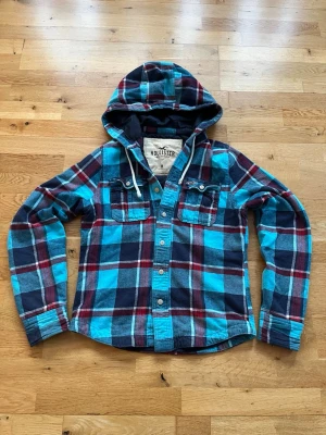 Hollister vintage Skjorta/tröja - Säljer nu denna otroligt snygga vintage Hollister  Skjortan med rutigt mönster. Hoodien är i storlek M och modellen på bilden är 183 och väger 67 kilo. Denna tröja  har fodrat material på insidan vilket gör den extra varm och skön!   Tröjan har inga defekter.  Priset är inte hugget i sten. Skriv gärna om ni har mer funderingar 😊