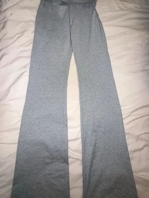 Grå yogabyxor - Säljer ett par ljusgrå yogabyxor med bred linning och utsvängda ben. Byxorna är i mjukt och stretchigt material, perfekta för chill dagar hemma eller när du vill vara extra bekväm. Inga synliga loggor eller detaljer, enkel och clean look.