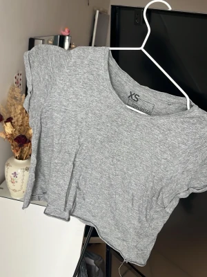 Grå croppad t-shirt  - En enkel och stilren grå croppad t-shirt från Sinsay. T-shirten har korta ärmar, rund halsringning och är tillverkad i mjuk bomull. Perfekt till jeans eller kjol för en avslappnad look.