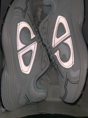 Vita Dior B30 sneakers - Snygga grå Dior B30 sneakers med reflekterande detaljer på sidan och robust sula. Skorna har en modern siluett med mesh och syntetmaterial för en sportig vibe. Tydlig Dior-logga på sulan och stora reflekterande paneler på ovandelen. Kartong nedkommer ej, pris kan diskuteras vid snabb affär. skorna ej äkta
