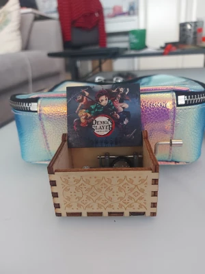 Demon Slayer speldosa i metall - Cool speldosa av anime-serien Demon Slayer, tillverkad i mörk metall. Levereras i en dekorativ trälåda med lasergraverat mönster. Perfekt för fans av serien som vill ha en unik dekoration som spelar introt från första säsongen 