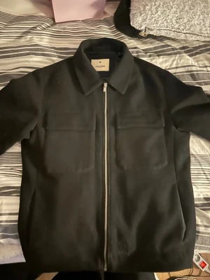 Svart overshirt från Jack & Jones - Stilren svart overshirt från Jack & Jones med klassisk krage. Jackan har en rak passform och dragkedja framtill. Materialet är mjukt och känns som ullblandning, perfekt för lager-på-lager. Enkel att matcha med olika outfits.