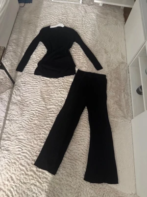 Svart ribbat set från LC Wakiki - Säljer ett svart ribbat set från LC Wakiki med långärmad topp och matchande byxor. Setet har en fin passform och är gjort i ett mjukt, stretchigt material som känns skönt mot huden. Tröjan har en fin slits som jag själv älskar och tycker är jätte fint. Perfekt för dig som gillar en stilren och enkel look.
