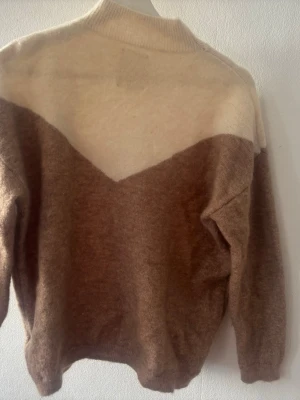 Beige och brun stickad tröja - (Köpte för 700 säljer för 200 )Mysig stickad tröja i beige och brun med V-formad färgövergång på bröstet. Tröjan har rund halsringning och långa ärmar. Materialet ser ut att vara mjukt och fluffigt, perfekt för kyligare dagar.