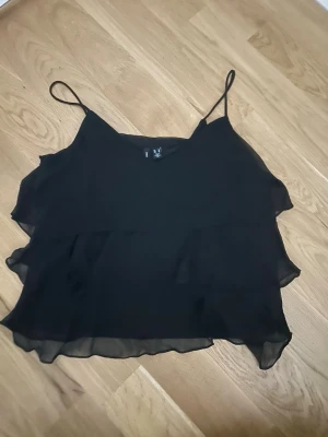 Svart linnetopp från Vero Moda - Säljer en svart linnetopp från Vero Moda med tunna axelband. Väldigt fin volang mönster. Säljer då jag endast använt den 1 gång och kommer inte använda igen.
