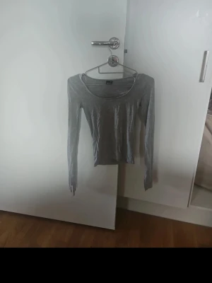 Grå långärmad topp  - En enkel och stilren grå långärmad topp från Gina. Toppen har rund halsringning och är tillverkad i mjuk bomullsmix som känns skön mot huden. Perfekt att matcha med jeans eller kjol för en clean look.
