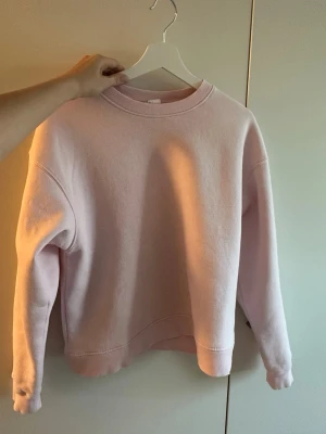 Ljusrosa sweatshirt  - En enkel och stilren ljusrosa sweatshirt med rund hals och ribbade muddar vid ärmslut och nederkant. Tröjan har en relaxed passform och är gjord i mjukt material, perfekt för att chilla eller hänga med kompisar.