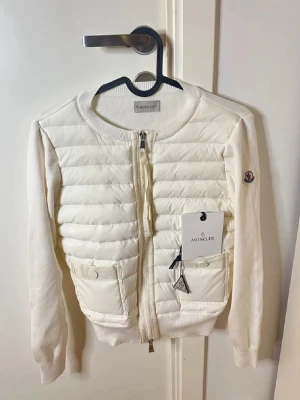 Vit quiltad cardiganjacka Moncler - Snygg vit cardiganjacka från Moncler med quiltad front och stickade ärmar. Jackan har två fickor med knappar, rund halsringning och dragkedja framtill. Moncler-logga på ärmen och exklusiv känsla i materialet. Pris kan diskuteras vid snabb affär 💕💕