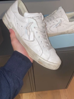 Vita Philippe Model sneakers - Snygga vita sneakers från Philippe Model med klassisk låg profil och lädermaterial. Skorna har vita snören, diskret logotyp på sidan och en robust sula som ger en clean look. Perfekta för dig som gillar stilrena och trendiga skor.