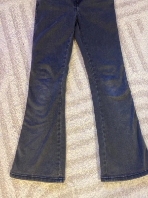 Mörkblå bootcut jeans - Säljer ett par mörkblå bootcut jeans med klassiska fickor och knappdetalj bak. Jeansen har en utsvängd passform och är tillverkade i denim. Perfekta för dig som gillar en retrostil och vill ha något som sticker ut. Har dock tappat lite färg på båda knapparna där bak!!
