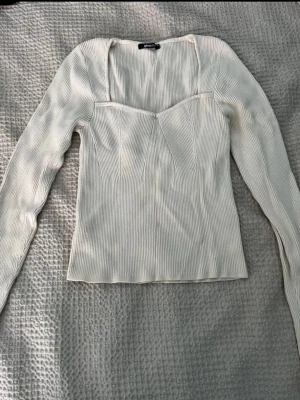 Vit ribbad långärmad topp - Säljer en stilren vit ribbad topp med lång ärm och fyrkantig urringning. Toppen har en figurnära passform och är tillverkad i ett stretchigt material som känns mjukt mot huden. Perfekt att matcha med jeans eller kjol för en clean look.