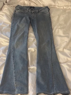 True religion jeans  - Ett par klassiska blå bootcut jeans med låg midja och fem fickor. Jeansen har en lätt tvättad look och är tillverkade i denim med en skön passform. Perfekta för en avslappnad och trendig stil.