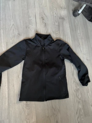 Svart vindjacka med dragkedja - Svart sportjacka från SOC med hel dragkedja och hög krage. Tröjan har långa ärmar, två sidofickor med dragkedja och en liten vit logga på ryggen. Materialet är lätt och smidigt, perfekt för träning och utomhusaktiviteter. Använd fåtal gånger. Säljer för att den är för liten, pris går att diskutera🫶🏻