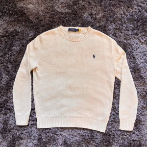 Beige stickad tröja från Polo Ralph Lauren - Snygg beige stickad tröja från Polo Ralph Lauren med klassisk rund halsringning och broderad logga i mörkblått på bröstet. Perfekt till kallar sommarkvällar. Mycket bra skick. Storlek S hör av er vid intresse!!