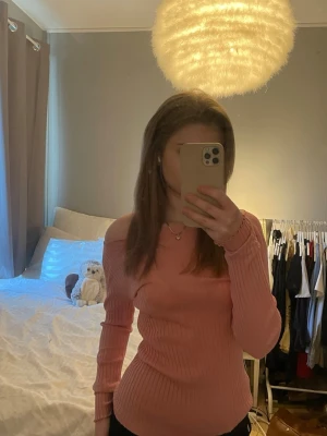Rosa off shoulder stickad tröja - Säljer en snygg rosa stickad tröja med off shoulder-design och långa ärmar. Tröjan har ribbade detaljer vid midjan och ärmslut, vilket ger en cool och modern look. Perfekt för dig som vill ha något trendigt och bekvämt.