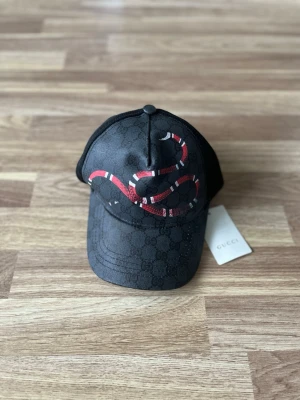 Svart keps med röd orm på - En svart keps med en röd orm på. Skickar snabbt! Pris går att diskuteras. 