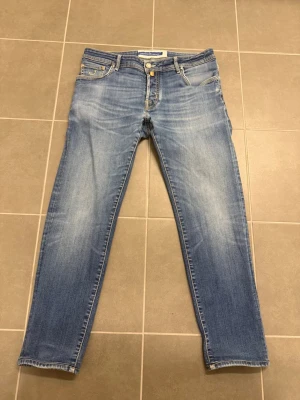 Ljusblå raka jeans från Jacob Cohen W35 - Säljer ett par ljusblå jeans från Jacob Cohen med raka ben och klassisk femficksmodell. Jeansen har snygga slitningar och kontrastsömmar, samt knappgylf. Perfekta för en avslappnad och trendig look.