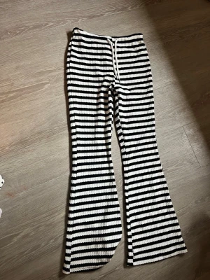 Randiga stickade byxor med utsvängda ben - Snygga stickade byxor med svartvita horisontella ränder och utsvängda ben. Byxorna har en dragsko i midjan och är gjorda i ett mjukt, stickat material med struktur. Perfekta för en chill och trendig look i sommar