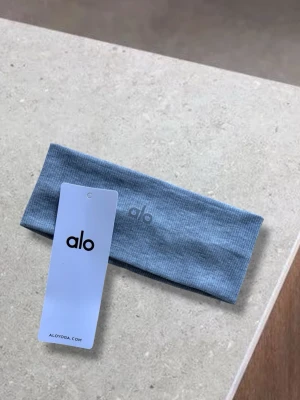 Grått hårband från Alo Yoga - Snyggt och stilrent grått hårband från Alo Yoga. Tillverkat i ett mjukt och stretchigt material som sitter bekvämt på huvudet. Perfekt för att hålla håret på plats.