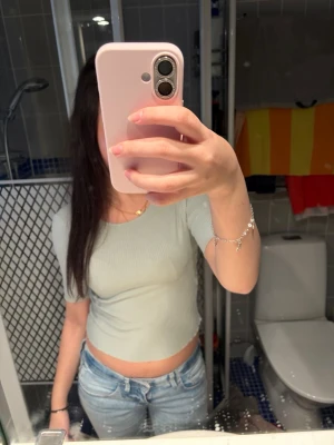 Ljusgrön croppad topp från Lindex - Säljer en ljusgrön croppad topp från Lindex i ribbad bomull. Toppen har korta ärmar och en tight passform som framhäver midjan. Perfekt att matcha med jeans eller kjol för en snygg look.