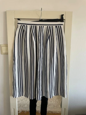 Kjol  .Stockholm lm - Säljer en snygg kjol  med vertikala marinblå ränder på vit botten. Kjolen har hög midja och ett lätt utställt fall som ger en klassisk och fräsch look. Har två sidor fickor.Perfekt för vår och sommar! Materialet känns mjukt och luftigt.