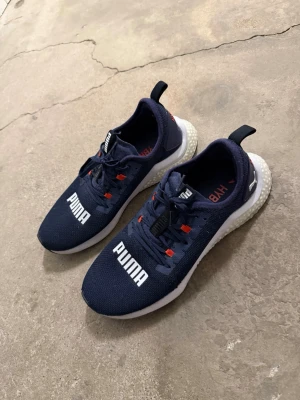 Mörkblå PUMA hybrids - Snygga mörkblå sneakers från PUMA med vit sula och tydlig PUMA-logga på ovansidan. Skorna har mesh-material för bra ventilation, röda detaljer vid snörningen och en pull-tab bak. Perfekta för dig som gillar sportig stil.