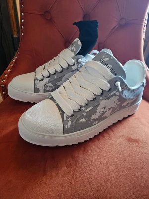 Gråvita sneakers från Numeris 44 - Snygga sneakers från Numeris i strl 44i grått och vitt med coolt camouflage-mönster. Skorna har breda vita snören, kraftig räfflad sula och detaljer i syntetmaterial. Perfekta för dig som vill sticka ut med en unik look. De är helt nya. 