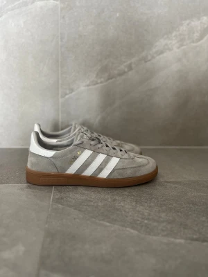 Adidas grå spezial sneakers med vita ränder - Snygga Adidas spezial skor i grå mocka med klassiska vita ränder på sidorna och brun gummisula. Har inte används en ändaste gång🫱🏻‍🫲🏼 Riktigt fräscha inför sommaren, pris kan diskuteras!💪🏼