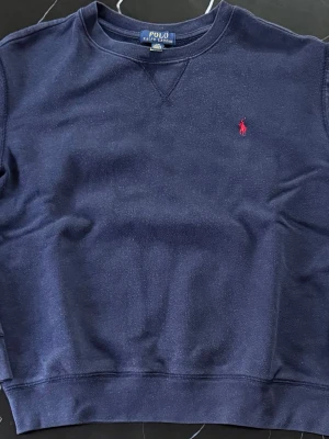 Polo Ralph Lauren navy blue sweater – red logo – S/M minimal fit - Polo Ralph Lauren sweater i mörk navy blue färg med röd broderad logga på bröstet. Stilren och eftertraktad modell som passar perfekt till både vardag och mer uppklädda outfits. Enkel att matcha och sitter bekvämt på kroppen – funkar lika bra med jeans som chinos. 📏 Mått: • Längd: 57 cm • Bredd (pit to pit): 50 cm 📌 Skick: väldigt bra skick, inga hål eller fläckar ✨ Detaljer: • Rund hals (crewneck) • Navy blue färg • Röd broderad logga • Mjuk och bekväm 💬 Skriv om du vill ha mer info 😊