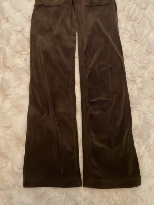 Bruna mjukisbyxor i velour Juicy Couture - Mörkbruna mjukisbyxor i mjuk velour från Juicy Couture. Byxorna har raka ben och broderad JC-logga vid fickan. Perfekta för en chill och avslappnad stil.storlek XXS Pris 70kr