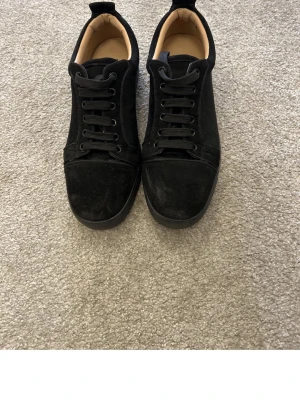 Svarta sneakers med röd sula - Stilrena svarta sneakers i mocka med svarta skosnören och en cool röd sula med textdetalj. Lågt skaft och klassisk design som passar till det mesta. Insidan är ljusbeige för en snygg kontrast. Perfekta för dig som gillar en clean look.