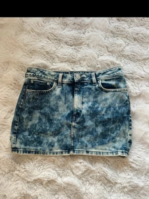 Blå acid wash jeanskjol från Monki - Cool kort jeanskjol från Monki i blå acid wash med klassiska fickor fram och bak samt bälteshällor. Kjolen har en knapp och dragkedja framtill och är perfekt för dig som gillar en edgy och trendig look. Strl 38 men liten i storlek