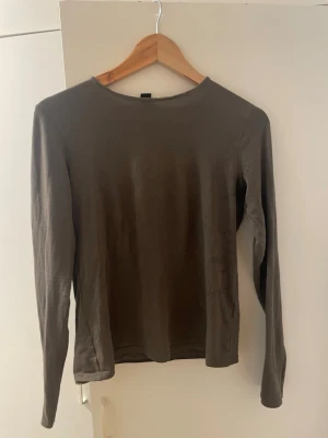 Grønn långärmad topp i bomull - En enkel och stilren brun långärmad topp i mjuk bomull. Modellen är slim och har en rund halsringning, perfekt att matcha med jeans eller kjol. Passar dig som gillar basic och tidlösa plagg.