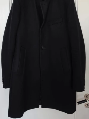 J.Lindberg melton rock - Stilren svart rock med rak passform och diskreta fickor framtill. Rocken har en enkel knäppning med en knapp och en bröstficka. Materialet är ull, vilket gör den perfekt för kyliga dagar. Passar dig som gillar en tidlös och elegant look.