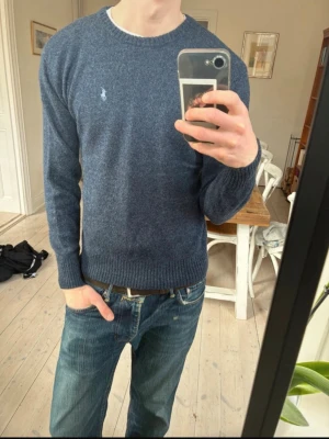 stickad tröja Ralph Lauren - Mörkblå stickad tröja från Polo Ralph Lauren med rund halsringning och diskret broderad logga på bröstet. Tröjan har långa ärmar och ribbade muddar vid ärmslut och nederkant. Perfekt till våren och sommaren, strl S