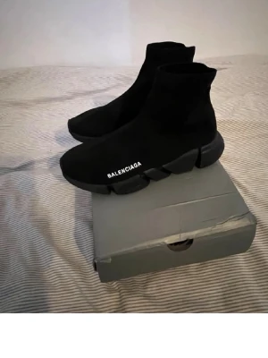 Balenciaga Speed Trainer svarta sneakers - Svarta Balenciaga Speed Trainer sneakers med stickad ovandel och chunky sula. Logotypen är tryckt i vitt på sidan. Skorna har en strumpliknande passform och är tillverkade i textilmaterial med gummisula. Perfekt för dig som gillar en clean och modern look.
