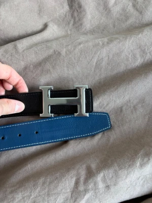Hermes bälte  - Hermes bälte i längden 105cm. Fint skick. Använd några gånger. Man kan ändra färgen mellan svart och blå.