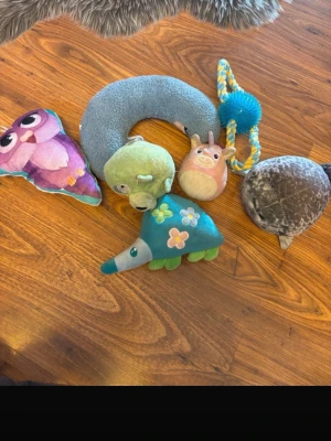 Samling mjuka djurleksaker - Säljer en samling mjuka djurleksaker i olika färger och former, bland annat en rosa uggla, grön krokodil, blå myrslok med blommor och en grå säl. Materialet är plysch och tyg, vissa har broderade detaljer och en har ett rep med boll.