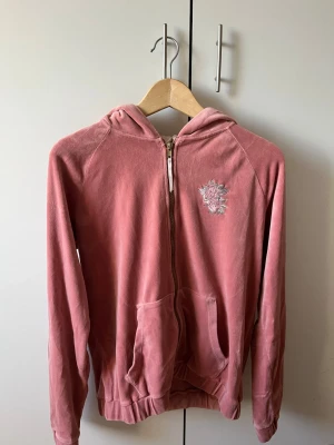 Rosa hoodie med broderi och dragkedja  - Rosa hoodie i mjukt velourmaterial med dragkedja framtill. På ryggen finns broderier av blommor och fåglar. Hoodien har en guldfärgad huva💕💕