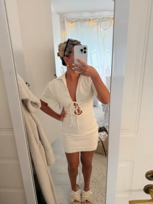 Zara Vit kortklänning med snörning - Säljer en vit kortklänning med krage och djup v-ringning. Klänningen har snörning framtill i midjan och korta ärmar. Snygg och trendig modell som ger en fräsch look. Perfekt för dig som gillar stilrena detaljer och vill sticka ut.