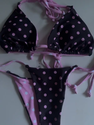 Svart och rosa prickig bikini - Snygg bikini med svart bas och ljusrosa prickar. Både överdel och underdel har knytband för justerbar passform. Underdelen har även en rosa insida med svarta prickar. Perfekt för strandhäng eller poolparty!