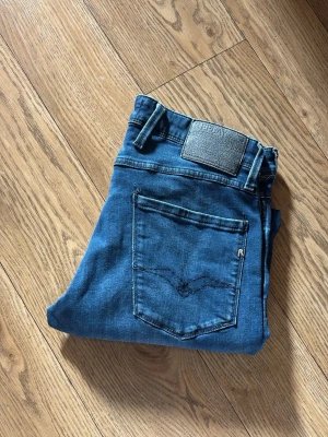 Blå jeans från Replay - Snygga blå jeans från Replay med klassisk femficksdesign och tydlig logotyp på bakfickan samt läderpatch i midjan. Jeansen har raka ben och är tillverkade i ett mjukt denimtyg som ger en skön passform. w32 L32