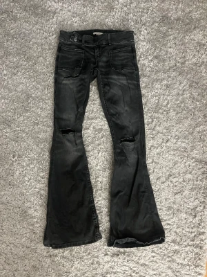Svarta bootcut jeans med slitningar/dżinsy - Säljer ett par svarta bootcut jeans med slitningar på knäna och lätt tvättad look. Jeansen har fem fickor och utsvängda ben, vilket ger en retro och trendig vibe. Perfekta för dig som gillar en avslappnad och edgy stil.