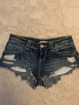 Blå lågmidjade jeansshorts  - Säljer ett par blå jeansshorts från Gina Tricot med slitningar framtill. De är lågmidjade och sitter väldigt fint på. Säljer då de är för små för mig. Mycket bra skick.