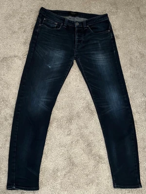 Svarta slim fit jeans - Snygga svarta slim fit jeans med lätt tvättad look och klassiska fem fickor. Jeansen har en smal passform och subtila slitningar framtill. Perfekta för en trendig och avslappnad stil.