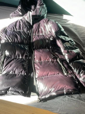 Glansig svart dunjacka från Moncler - Säljer en glansig svart dunjacka från Moncler med huva och dragkedja framtill. Jackan har två fickor med dragkedja och Moncler-logga på ärmen. Perfekt för kalla vinterdagar och riktigt snygg streetstil. De går att skanna, vid snabb äffar kan jag dra ner på priset.