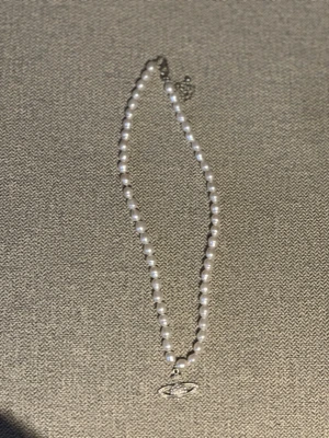 Vivienne Westwood pärlhalsband - Snyggt halsband från Vivienne Westwood med vita pärlor och det ikoniska orb-hänget i silverfärg. Perfekt statement-piece med klassisk och trendig vibe. Kedjan har justerbar längd och pärlorna är jämnt placerade runt hela halsbandet.