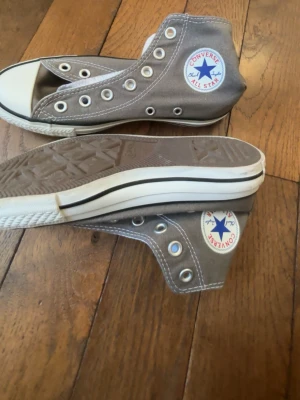 Grå Converse All Star höga sneakers - Klassiska Converse All Star sneakers i grå canvas med vita gummisulor och tåhätta. Utan snören!