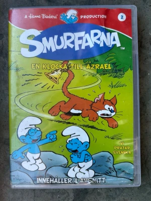 Smurfarna - en klocka till Azrael dvd - Innehåller 4 avsnitt: Hogathas hjärtklappning & En klocka till Azrael, Smurfarnas Halloween, En magisk skälla & folk och Smurf, Smurfen som ville vara kung & Skönhet är bara smurfig. Speltid: 95 minuter. Utgivningsår: 2011.   Finns på språk: Svenska, Danska, Norska   OBS!! skivorna är begagnade så det kan förekomma repor/hairlines på skivorna, men då jag kollar igenom alla filmer jag säljer garanterar jag att alla funkar felfritt om inget annat står! :)